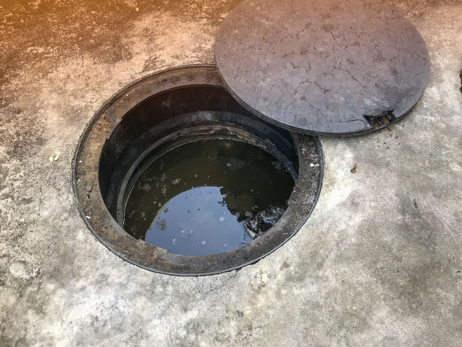 Åben rund kloakbrønd med låget lagt til side på en betonflade