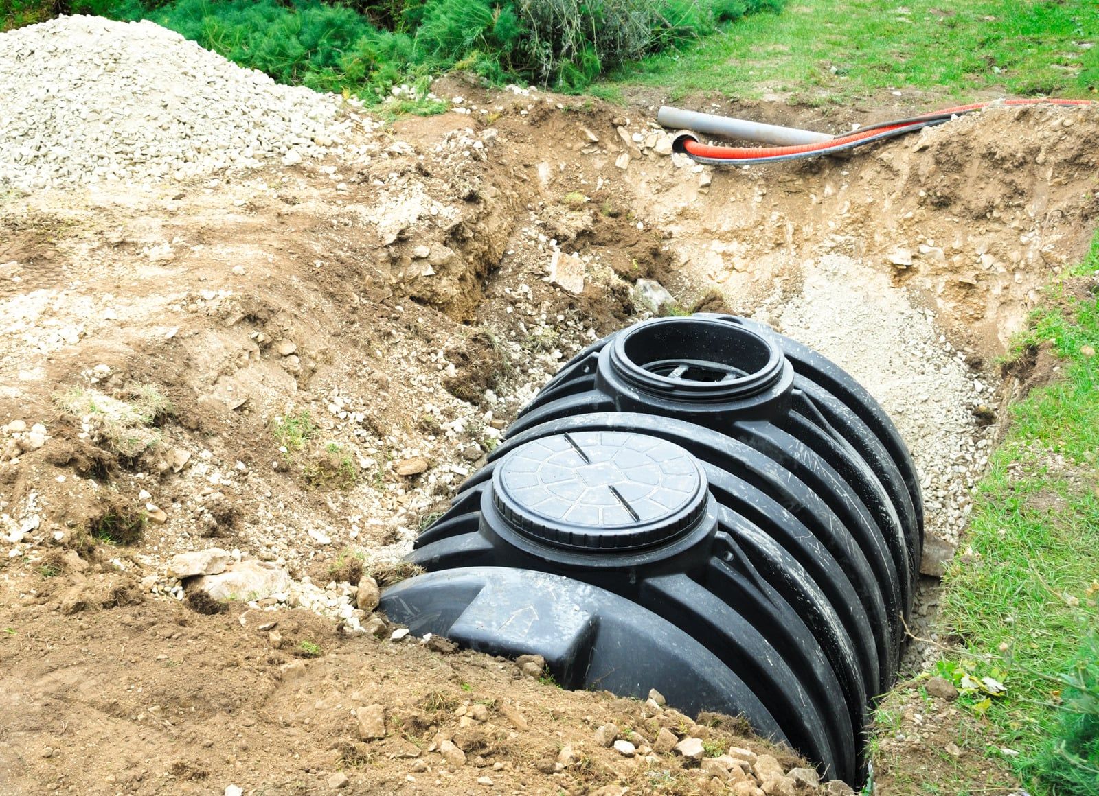 Sort plastseptiktank ligger i et udgravet hul klar til at blive tilsluttet