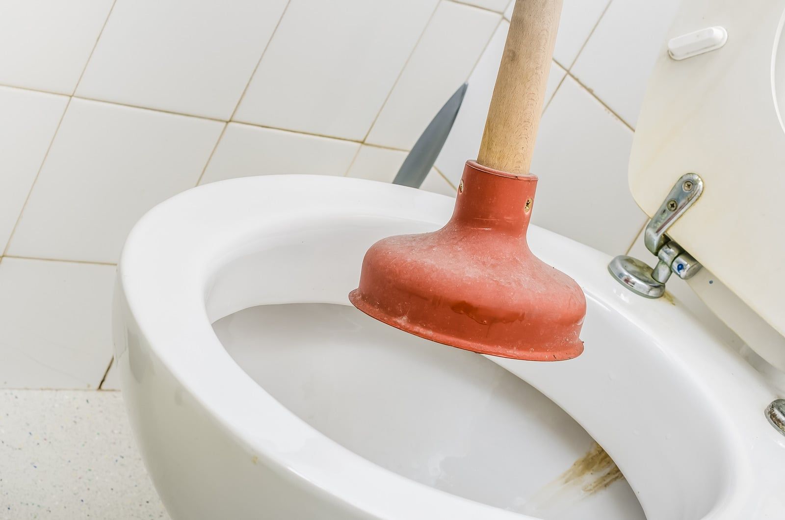Rød toiletsuger med træskaft står i et hvidt toilet